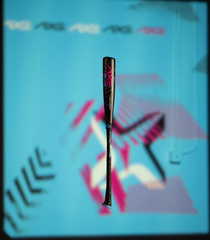 A black 2024 AXE Avenge Pro 3 Hybrid (-8) USA Baseball Bat (L174M), with pink and blue accents, is centered on a bright blue background featuring geometric shapes and abstract patterns in pink, white, and black.