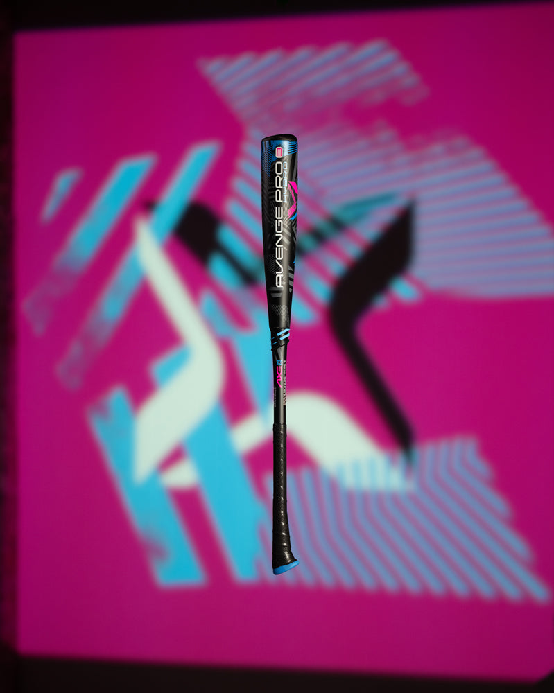 The 2024 AXE Avenge Pro 3 Hybrid (-8) USA Baseball Bat (L174M) stands upright against a vibrant backdrop of abstract pink, blue, white, and black geometric shapes and lines.