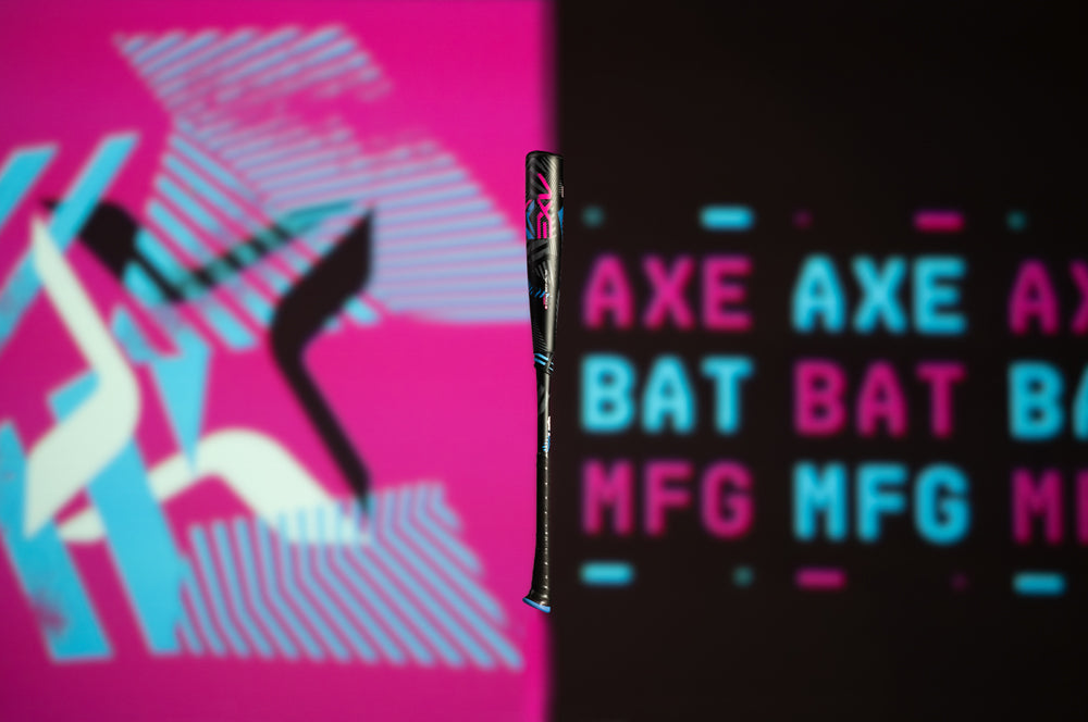 The 2024 AXE Avenge Pro 3 Hybrid (-8) 2 5/8" USA Baseball Bat by AXE stands upright, centered on a split background—pink with abstract lines on the left, black with “AXE BAT MFG” in blue and pink text on the right.