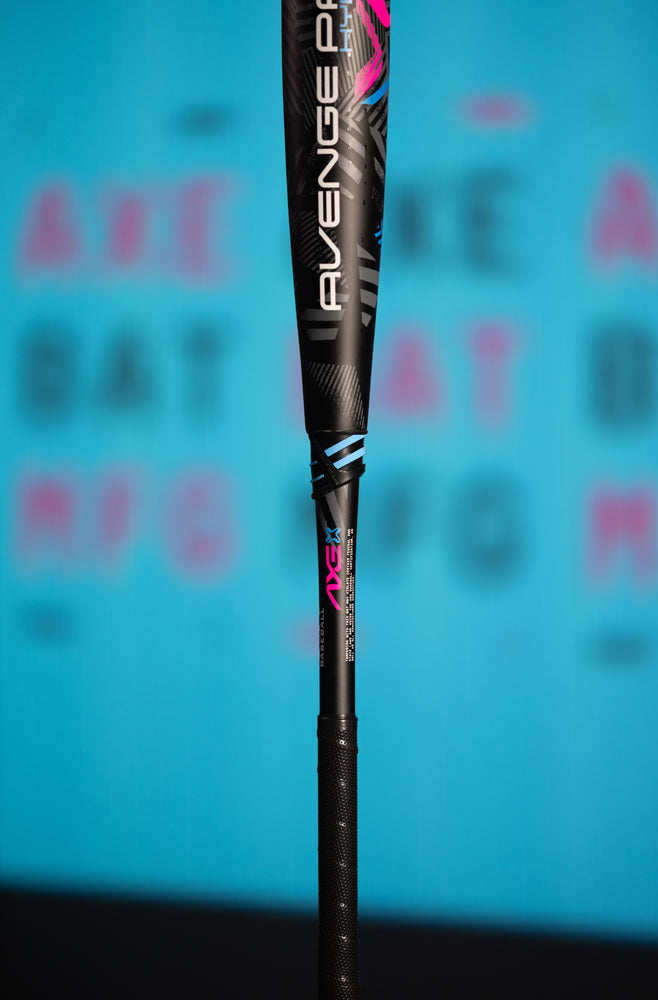 A close-up of the 2024 AXE Avenge Pro 3 Hybrid (-8) USA Baseball Bat (L174M), with pink and blue accents, upright against a blurred blue background featuring pink text.