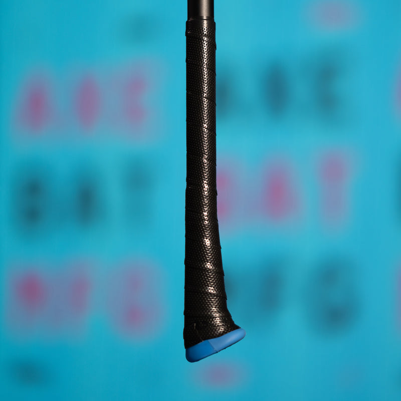 Close-up of a black, textured bat handle with a blue knob against a blurred blue background featuring large, indistinct letters in pink and black.