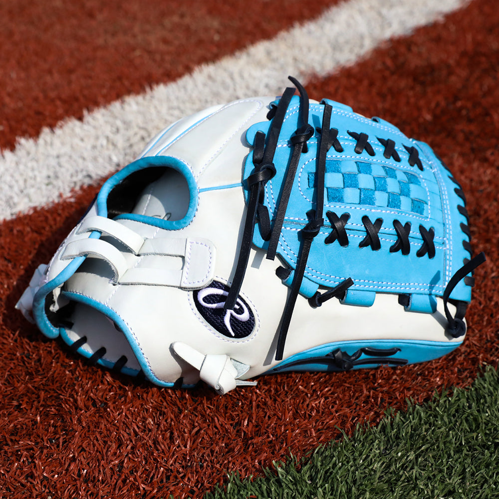 A white and blue baseball glove with black laces lies on artificial turf next to a white boundary line.