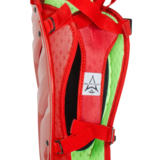 Close-up of a red and green shin guard with black straps and a visible white label reading DELTAFLEX. The padding is green, and the outer shell is red with textured detailing.