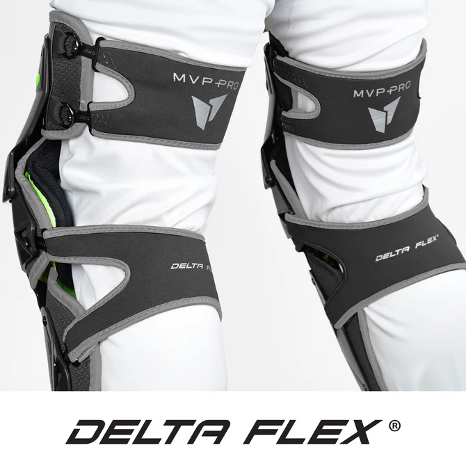 Close-up of a person wearing two black and gray All Star MVP Pro Catcher's Leg Guards: LG-5 over white pants, highlighting the pivoting hinge system for superior adult knee support.