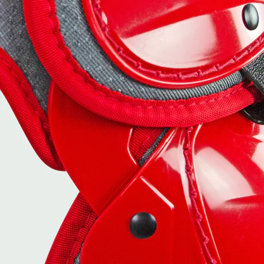Close-up of shiny red plastic protective gear with black rivets and gray fabric trim, likely part of sports equipment such as knee or elbow pads.