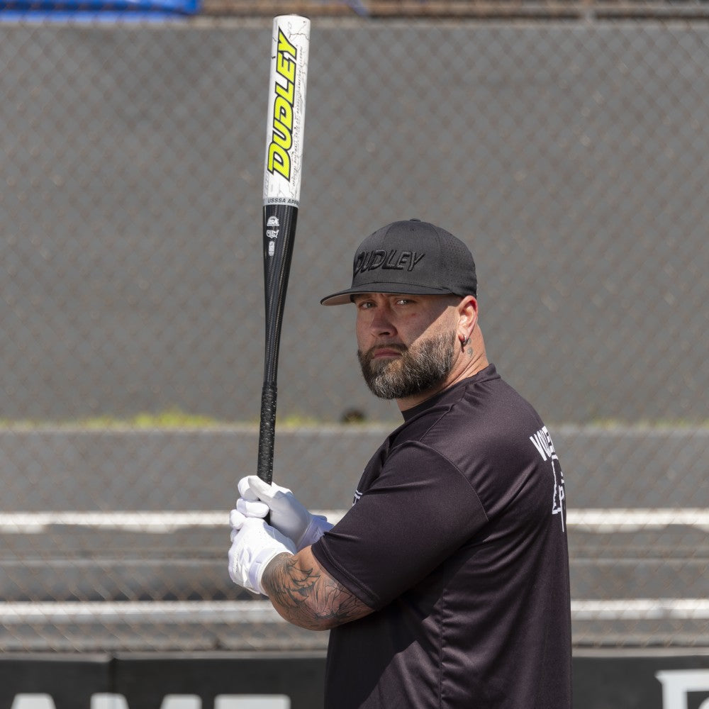 A man in a black shirt and cap holds a 2026 Dudley Lightning Legend 12″ Endloaded NSA USSSA Slowpitch Softball Bat: LLESPU over his shoulder.