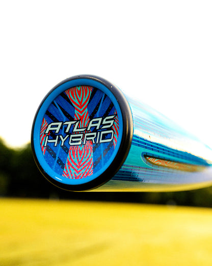 Close-up of the end cap on the Louisville Slugger 2027 Atlas Hybrid (-3) BBCOR Baseball Bat (WBL4246010), showing a colorful design with "Atlas Hybrid" text. The background features blurred grass and trees under a bright sky.