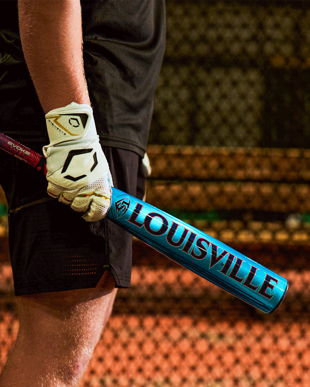 A person in a white glove holds the 2027 Louisville Slugger Atlas Hybrid (-3) BBCOR Baseball Bat (WBL4246010) on a baseball field with a chain-link fence in the background.
