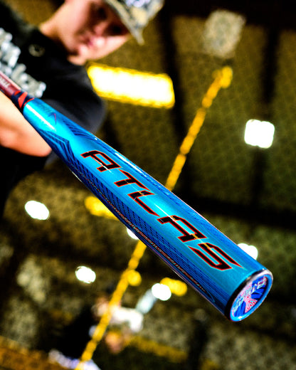 A person holds the 2027 Louisville Slugger Atlas Hybrid (-3) BBCOR Baseball Bat (WBL4246010), showcasing the blue EVOKE Alloy Barrel and red ATLAS letters, with an indoor batting cage blurred in the background.