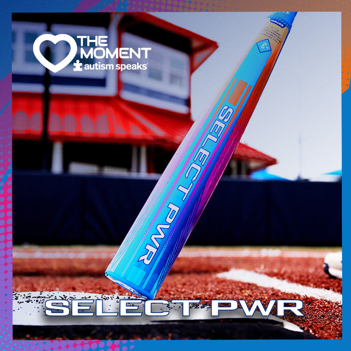 A close-up of the 2026 Louisville Slugger Select PWR Love the Moment (-3) BBCOR Baseball Bat (WBL4181010) rests on a field, with blurred stands and a building behind. The Autism Speaks logo appears in the upper left corner.