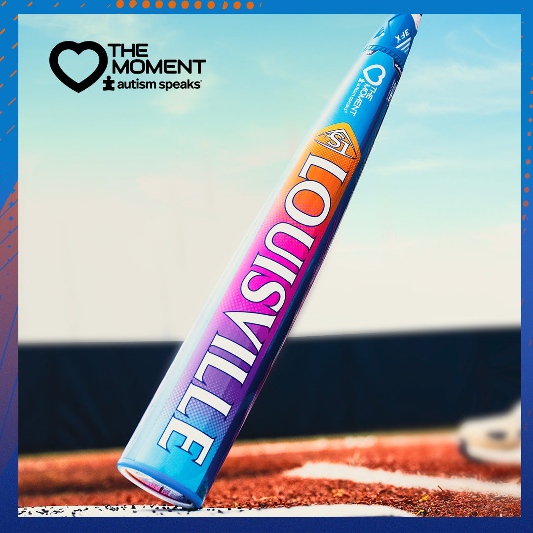 A brightly colored 2026 Louisville Slugger Select PWR Love the Moment (-3) BBCOR Baseball Bat lies on the ground, featuring a blue, orange, and purple gradient. In the corner, the Autism Speaks logo and "THE MOMENT autism speaks" text are displayed.