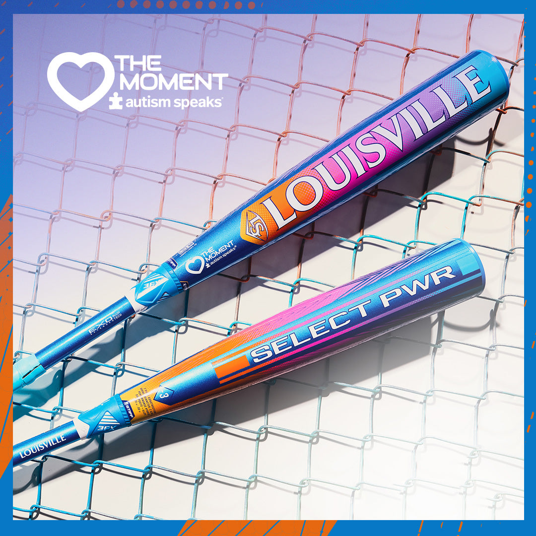 Two vibrant 2026 Louisville Slugger Select PWR Love the Moment (-3) BBCOR Baseball Bats (WBL4181010), featuring “LOUISVILLE” and “SELECT PWR,” rest on a teal chain-link fence, with Autism Speaks and The Moment logos in the top left.