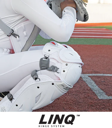 A catcher in white gear crouches on red turf, showcasing the All Star PHX Paige Halstead Fastpitch Catcher's Leg Guards (LGW-PHX) with LINQ hinge system and Delta-Flex calf harness. "LINQ HINGE SYSTEM" appears at the bottom of the image.