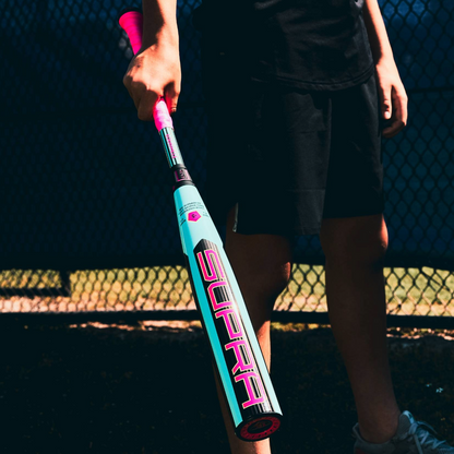 A person in black athletic wear holds the 2026 Louisville Slugger Supra (-5) USSSA Baseball Bat (WBL4120010) near a chain-link fence on a sunny day—the perfect gear for travel ball players.