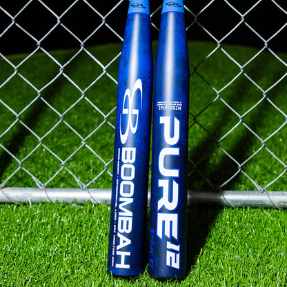 Two blue Boombah 2026 Pure12 Boom 12" Endloaded NSA USSSA slowpitch softball bats (M2B0-6142 RB) stand upright against a chain-link fence on bright green artificial turf.