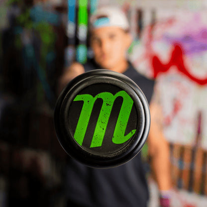 A person holds the 2026 Marucci CAT X RCKLESS Hybrid (-3) BBCOR Baseball Bat: MCBCRH (DEMO) toward the camera, highlighting the bright green M logo on its barrel against a vibrant graffiti background. This Marucci bat truly stands out.