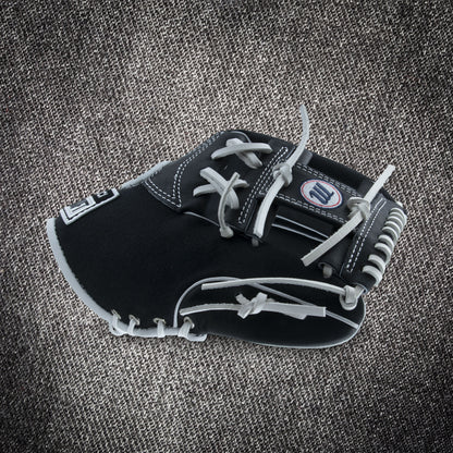 The Marucci NightShift CHUCK T 11.5" Baseball Glove (MFGNTSHFT-0103) in black and gray with white stitching and laces is shown on a textured gray fabric background.