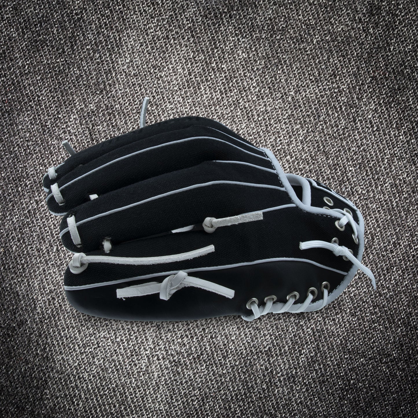 A Marucci NightShift CHUCK T 11.5" Baseball Glove (MFGNTSHFT-0103) from Marucci with white laces is shown closed on a textured gray surface.