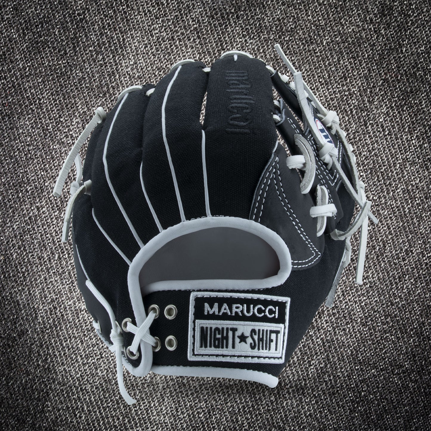 The Marucci NightShift CHUCK T 11.5" Baseball Glove (MFGNTSHFT-0103), black with white laces and gray accents, is shown on a textured gray background, displaying MARUCCI, NIGHT SHIFT, and Glove Cowboy patches.