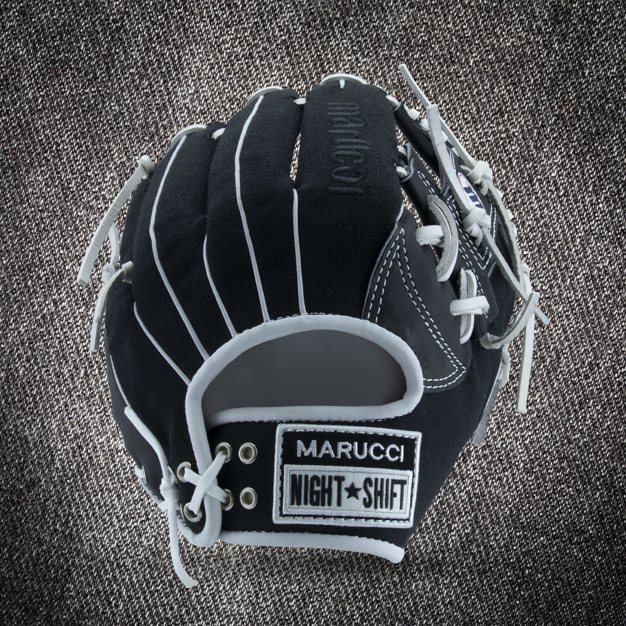 The Marucci NightShift CHUCK T 11.5" Baseball Glove (MFGNTSHFT-0103), black with white laces and gray accents, is shown on a textured gray background, displaying MARUCCI, NIGHT SHIFT, and Glove Cowboy patches.