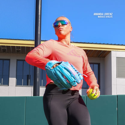 A softball player in sunglasses holds a Marucci NightShift Lorenz 12.5″ Fastpitch Glove: MFGNTSHFT-0305 and ball on a sunny field, with Amanda Lorenz Marucci Athlete text near her shoulder.