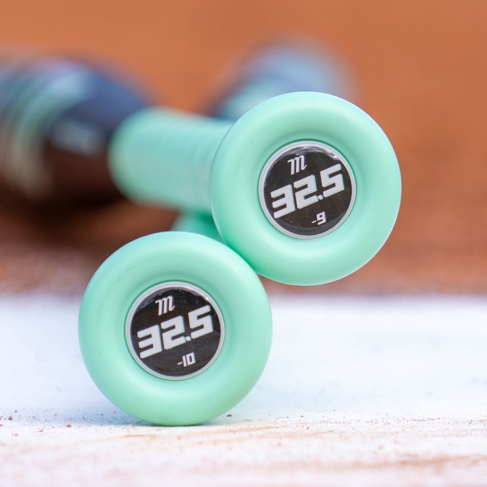 Close-up of two teal 2026 Marucci ASURA Lux (-10) Fastpitch Softball Bats (MFPASL10), labeled 32.5, with different weights (-10 and -9), resting on a baseball field.