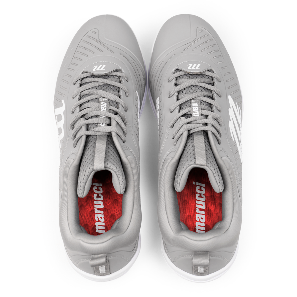 A pair of gray Marucci CFT Low Metal Cleats (MFWCTSL) is shown from above, with white Marucci logos on the sides and tongues, red insoles featuring white branding, gray laces, and textured detailing.