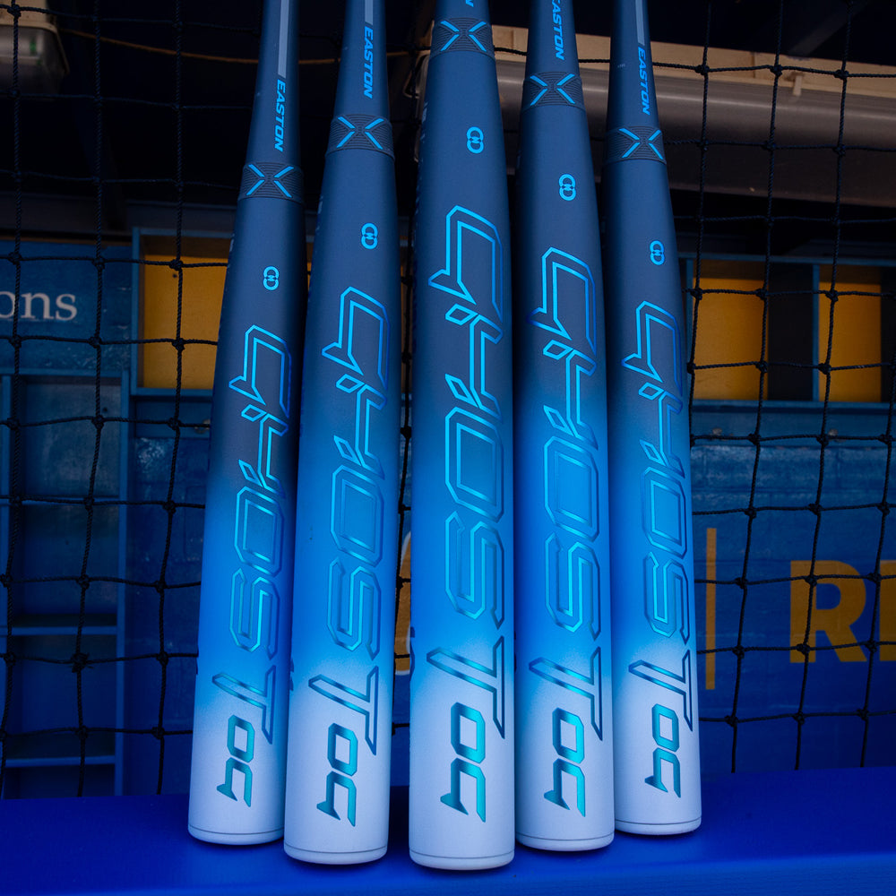 Five Easton Ghost OG (-11) Fastpitch Softball Bats (2025), featuring the brand’s signature Double Barrel construction, stand upright against a netted fence, showcasing the distinctive Easton design.