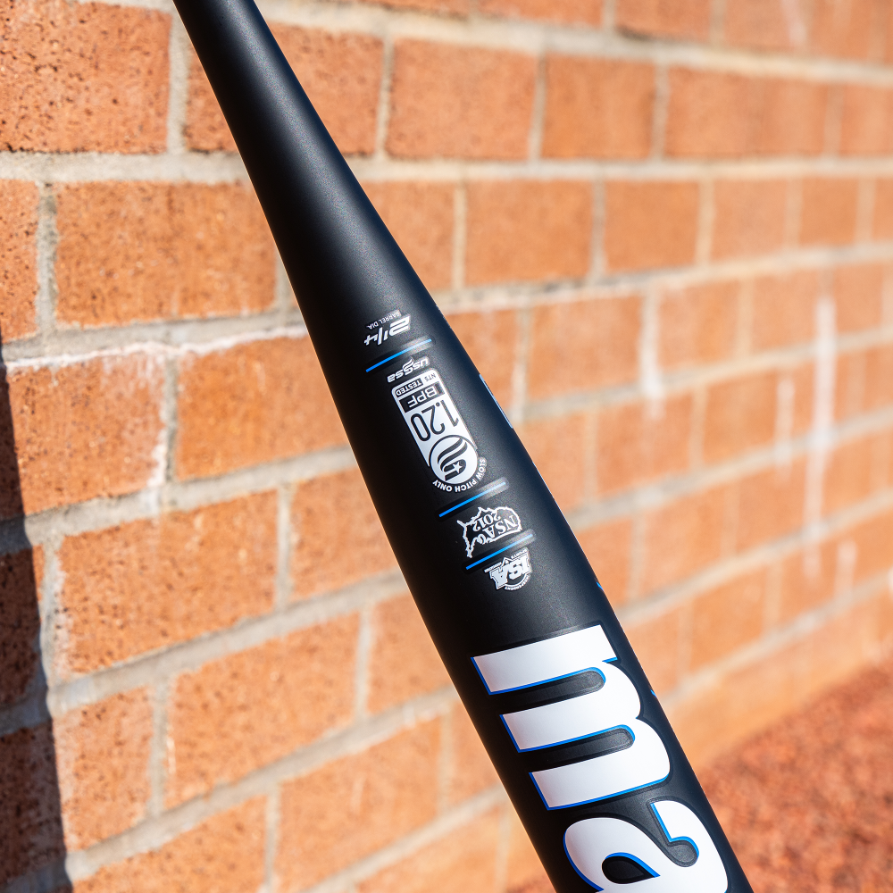 A close-up of a black 2025 Marucci Cypher 12.25" BH Load NSA USSSA Slowpitch Softball Bat (MSPC1BHU) against a brick wall, showing certification labels, part of the Marucci name in white, and Modulated Stiffness Technology.