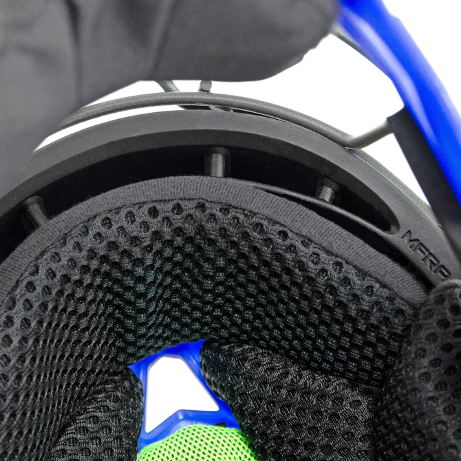 Close-up of the interior padding and mesh lining of a sports helmet, showing black, green, and blue segments, ventilation holes, and part of the helmets outer shell.