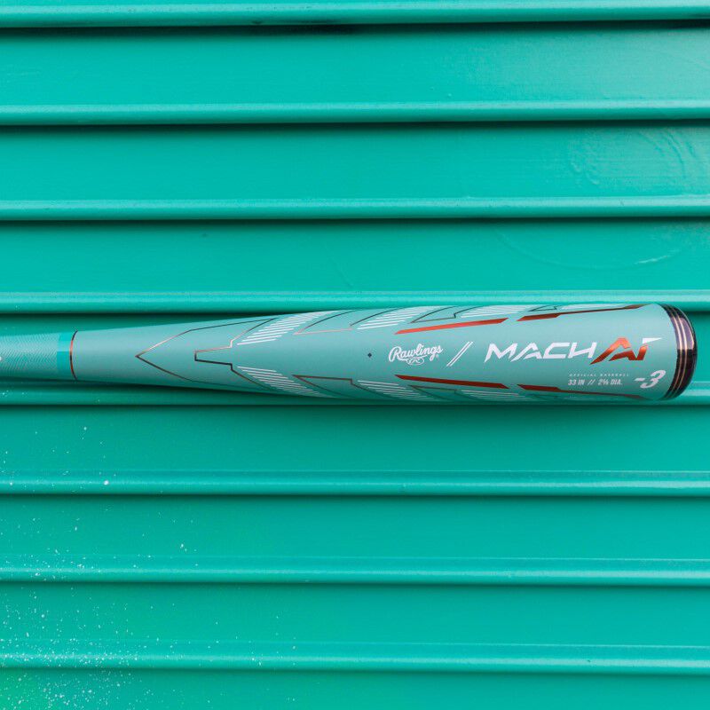 A 2024 Rawlings Mach AI (-3) BBCOR Baseball Bat: RBB4MC3 (USED), in teal with white and red accents, lies horizontally against a matching teal ridged surface.