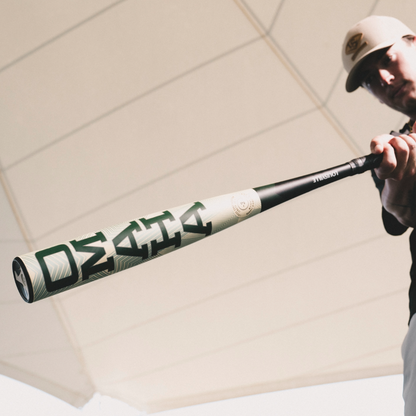 A baseball player in a cap showcases the Louisville Slugger Omaha (-3) BBCOR Baseball Bat (2026, WBL4117010), emphasizing its bold branding and one-piece alloy construction under a bright, white geometric canopy.