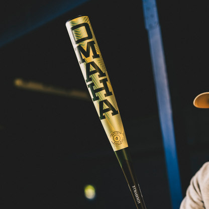 A close-up of the 2026 Louisville Slugger Omaha (-3) BBCOR Baseball Bat (WBL4117010) with “OMAHA” in bold and Louisville near the handle, held by a person in a tan hat against a dark, blurred background.