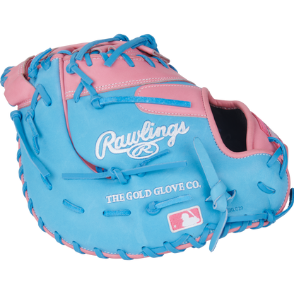 The Rawlings Heart of the Hide 12.25" First Base Mitt (PRORDCTU-10PCB) features a pink and blue design, blue laces, Rawlings branding, The Gold Glove Co. text, and an MLB logo stitched on the front.