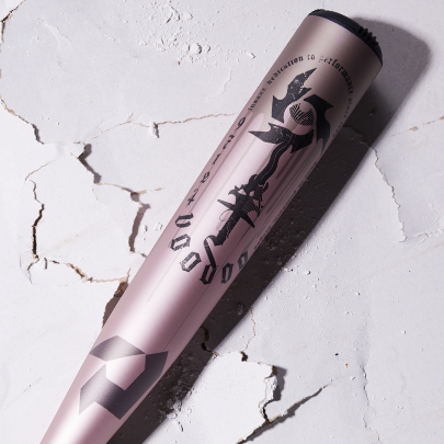 A metallic baseball bat with black graffiti-style designs and text lies on a cracked white surface, casting a shadow to the right.