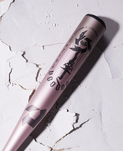 A 2025 DeMarini Voodoo One Rose Gold (-3) BBCOR Baseball Bat (WBD2628010) rests on a cracked white surface, its rose gold barrel and bold DeMarini graphics highlighted under bright light.