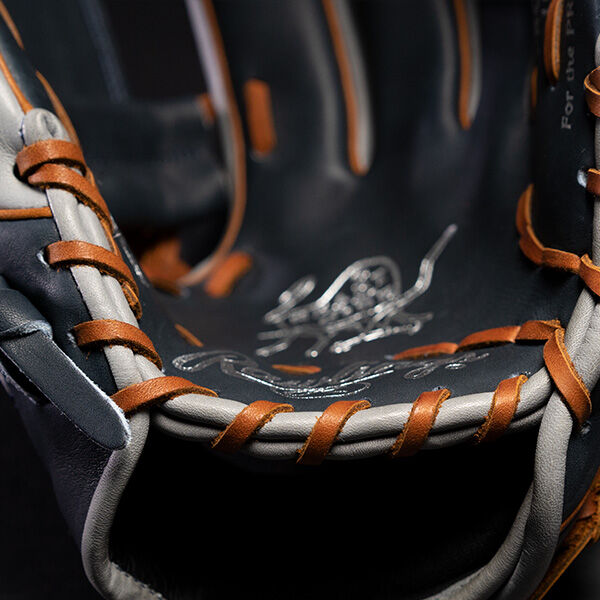 Close-up view of the inside of a baseball glove, showing detailed stitching and leather lacing in tan and gray tones, with embossed branding visible on the inner palm area.