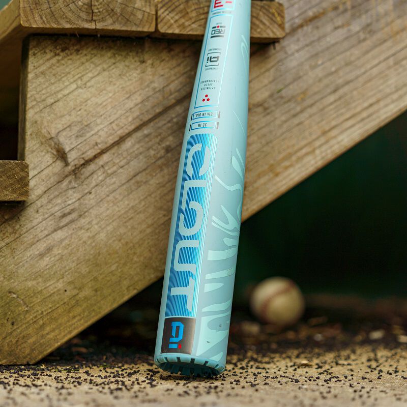 A close-up of a light blue 2025 Rawlings Clout AI (-3) BBCOR Baseball Bat: RBB5C3 (USED) by Rawlings leaning against wooden stairs, with a blurred baseball and scattered dirt in the background.