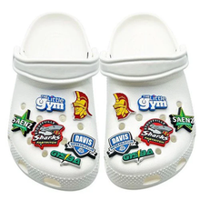 A pair of white Crocs decorated with DSG Apparel’s NSA Softball 3D Rubber Clog Charm and colorful jibbitz, featuring The Little Gym, a Trojan helmet, softball designs, and sports team badges.