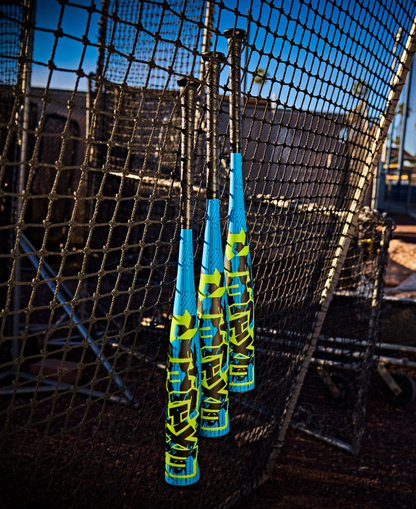 Three DeMarini 2027 Exile (-5) 2 3/4" USSSA Baseball Bats (WBD2716010), each with a one-piece design in blue and yellow, hang on batting cage netting with sports gear and fence visible beneath a clear sky.