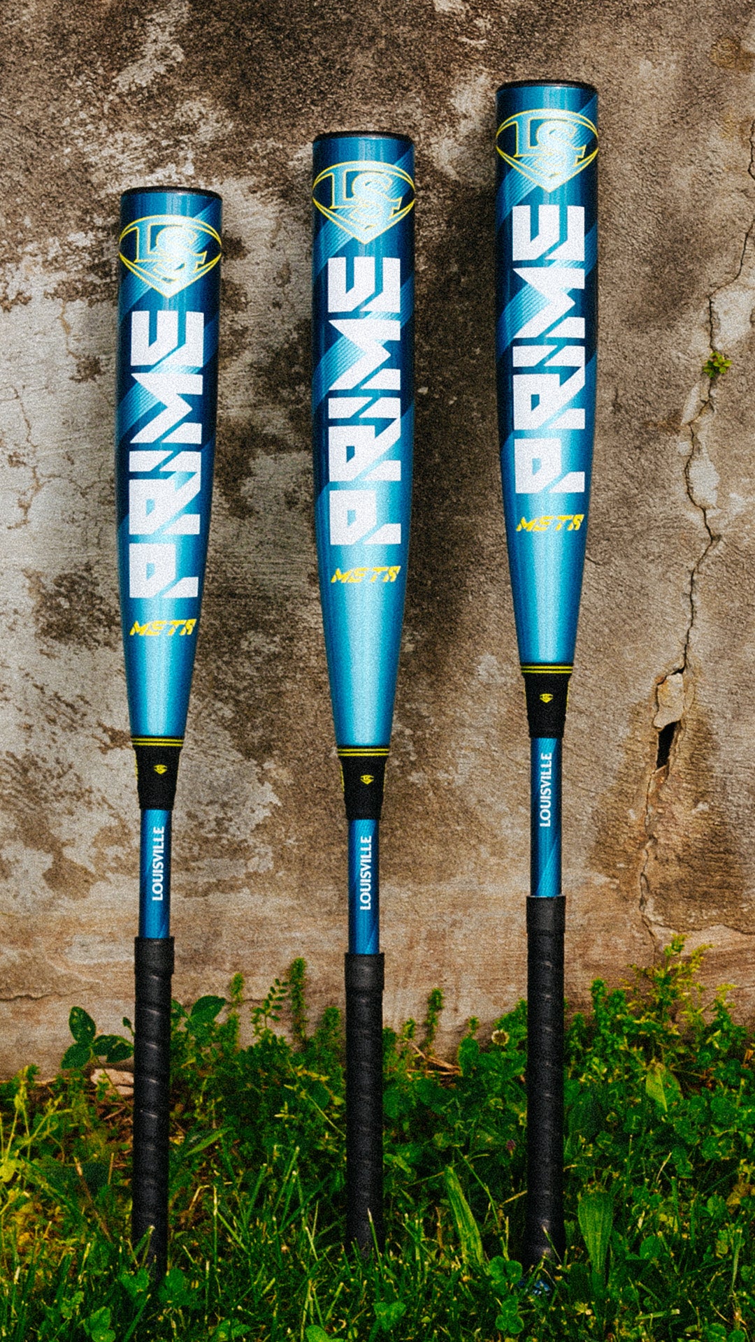 Three 2025 Louisville Slugger Meta Prime (-8) 2 3/4" USSSA Baseball Bats (WBL2971010 DEMO) stand upright on grass, displaying the Prime branding against a weathered concrete wall.