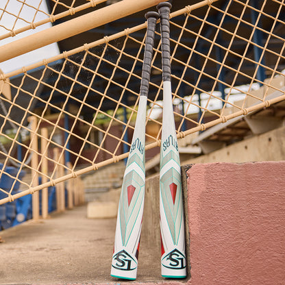 Two 2025 Louisville Slugger Atlas (-5) USSSA Baseball Bats with white, green, and red designs stand upright by a chain-link fence, highlighting the balanced one-piece alloy from Louisville Slugger.