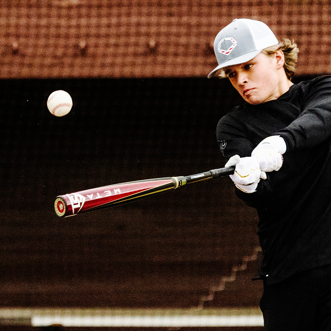 A young baseball player in a cap and black long-sleeve shirt swings a USED 2025 Louisville Slugger Meta (-3) BBCOR Baseball Bat (WBL2966010) during practice.
