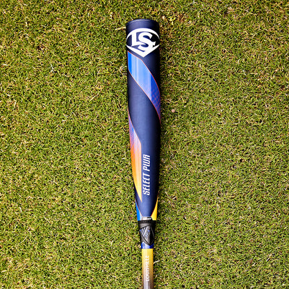 A 2025 Louisville Slugger Select PWR (-3) BBCOR Baseball Bat (WBL2967010) sits on the grass, its EXD Premium Alloy Barrel shining in the sunlight.