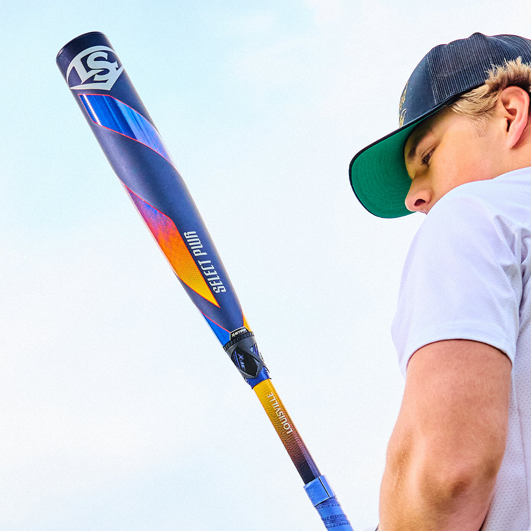 A person in a white shirt and black cap holds a Louisville Slugger 2025 Select PWR (-3) BBCOR Baseball Bat (WBL2967010 DEMO) over their shoulder, looking slightly upward with a blue sky in the background.