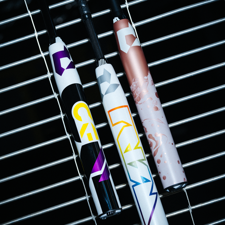 Three colorful, patterned vape pens with geometric designs rest side by side on a metal grid surface. The pens feature black, white, and rose gold color schemes with bold, modern graphics.