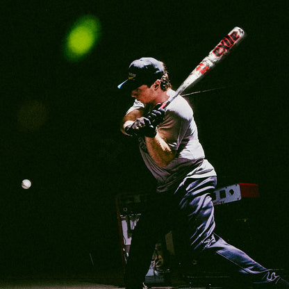 A man in athletic gear swings the 2026 DeMarini Exile (-3) BBCOR Baseball Bat (WBD2589010) by DeMarini, poised to hit a pitch under dramatic, low lighting.