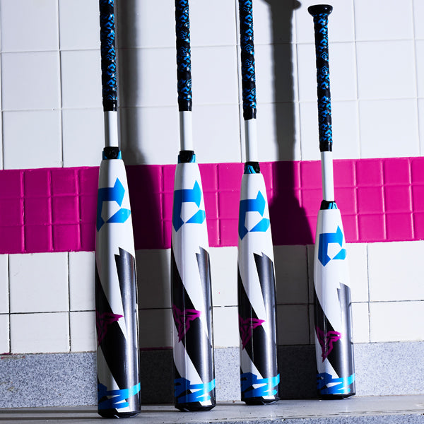 Four colorful baseball bats with blue, black, and white designs stand upright against a wall with white tiles and a broad horizontal pink stripe.