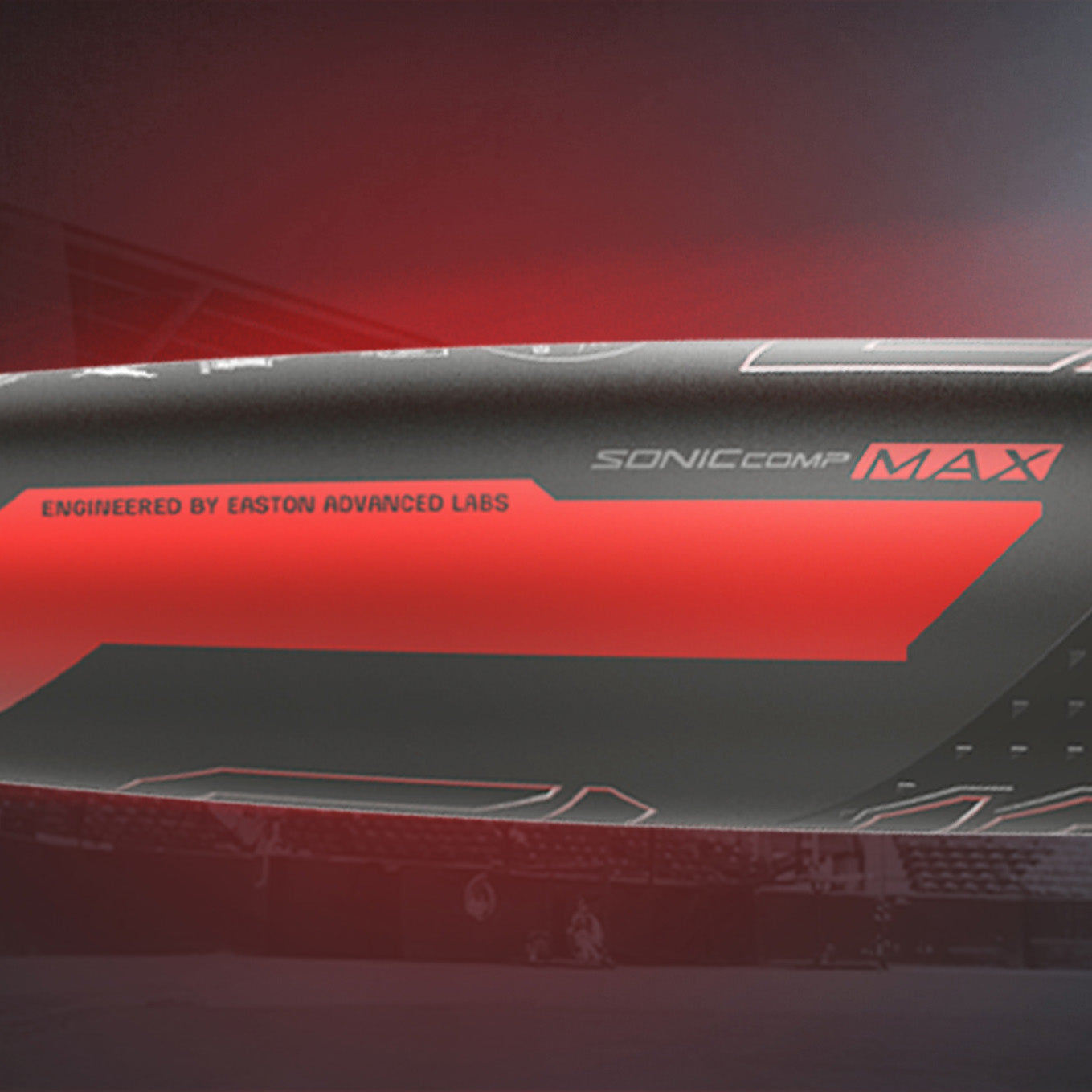 Close-up of a baseball bat labeled SONIC COMP MAX with Engineered by Easton Advanced Labs, featuring a sleek black and red design and a blurred stadium in the background.