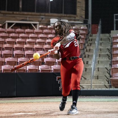 A softball player in a red uniform swings the 2026 Easton Ghost Advanced (-8) Fastpitch Softball Bat (EFP6GHAD8) by Easton, making contact with the ball as empty red stadium seats and a staircase appear in the background.